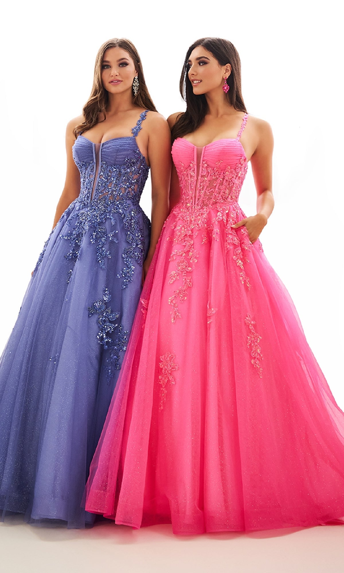 Two women stand side by side in stunning Ellie Wilde EW36202 floor-length gowns: one in a blue glitter tulle prom ball gown with floral embroidery, the other in pink with floral details and sheer corset bodice panels.